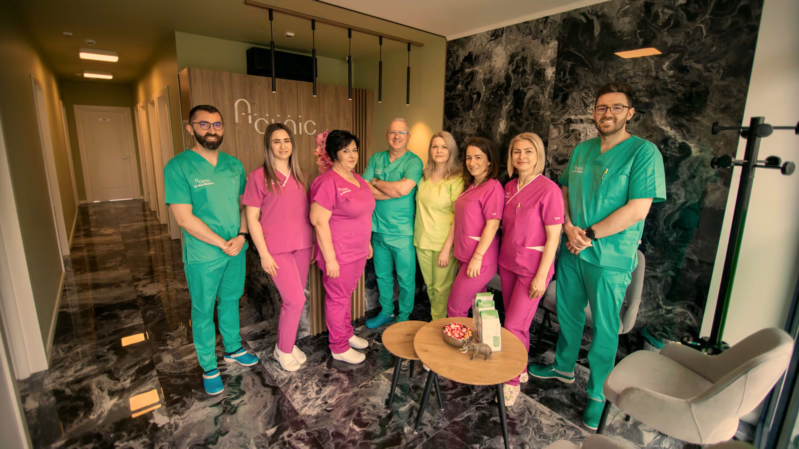Echipa A Clinic în holul clinicii din Baia Mare, în halate verzi și roz, lângă zona de așteptare