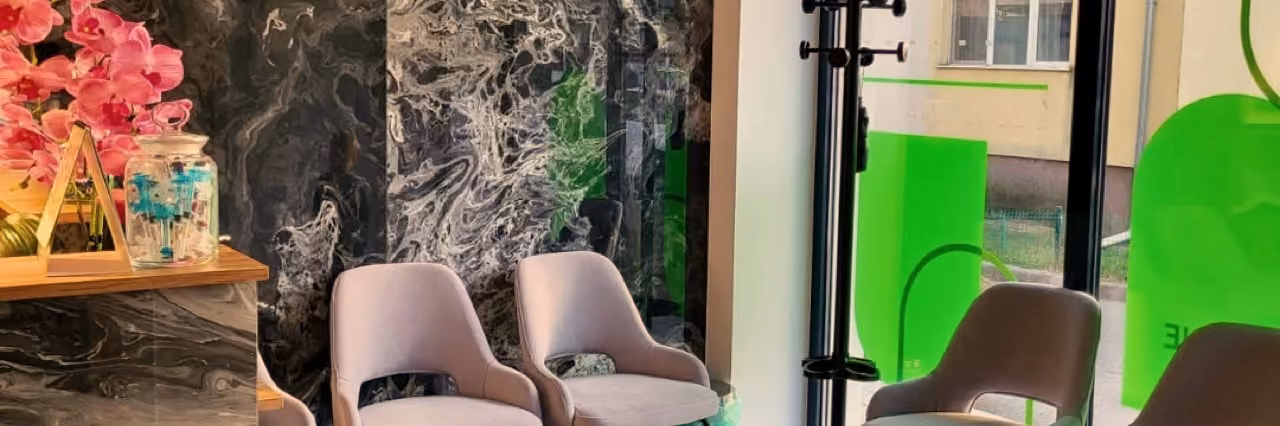 Sala de așteptare A Clinic, cu fotolii gri, perete de marmură închisă la culoare și lumină de la stradă