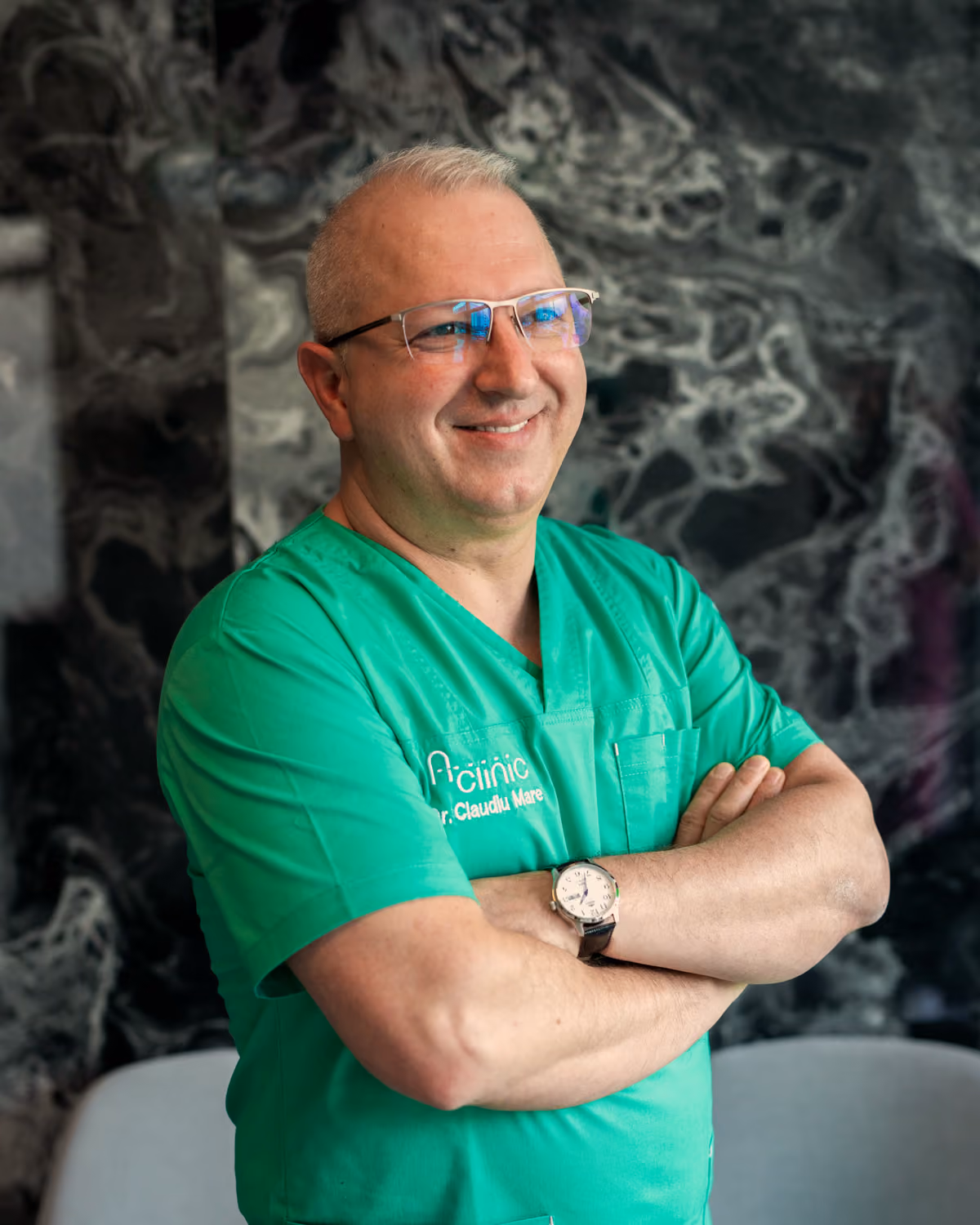 Dr. Claudiu Mare, medic primar chirurgie generală, în halat verde A Clinic, cu brațele încrucișate, în recepția clinicii