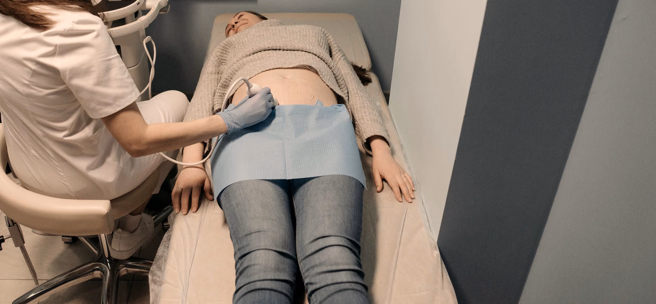Medic care efectuează o ecografie abdominală, cu pacienta întinsă pe patul de examinare