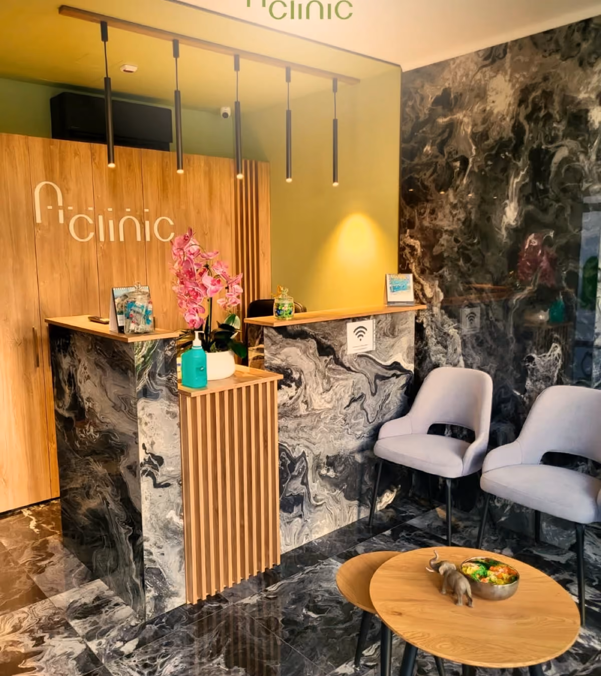 Recepția A Clinic, cu peretele de lemn, logoul clinicii și o orhidee albă